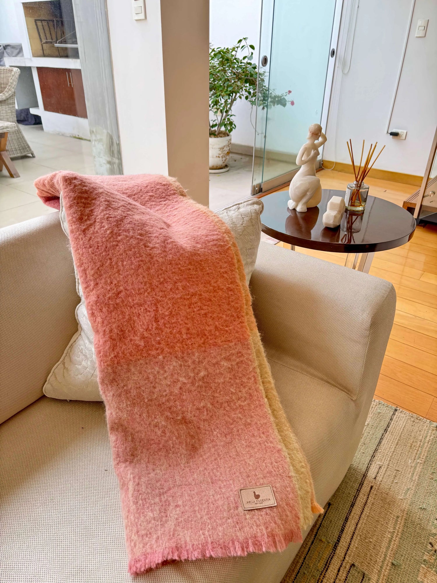 Manta de baby alpaca rosa Aklla Essentia sobre sofá, ejemplo de lujo sostenible y diseño atemporal.